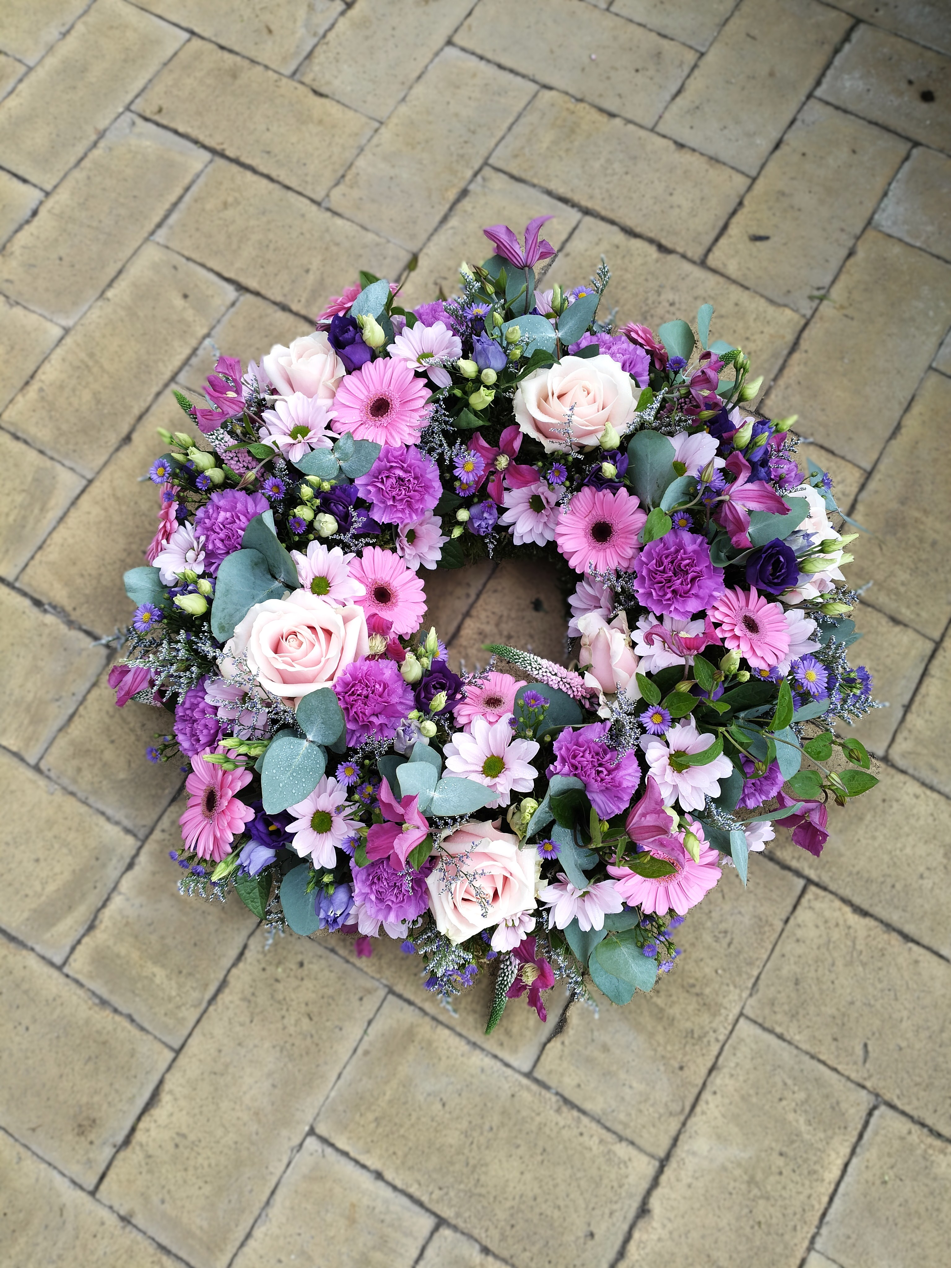 Rundpyntet krans med blomster i lilla og lyserøde nuancer. 