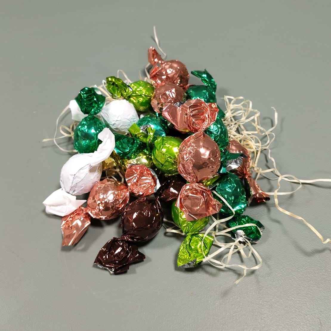 En bunke af chokoladekugler med rosa, grøn, brun og hvid skinnende papir.