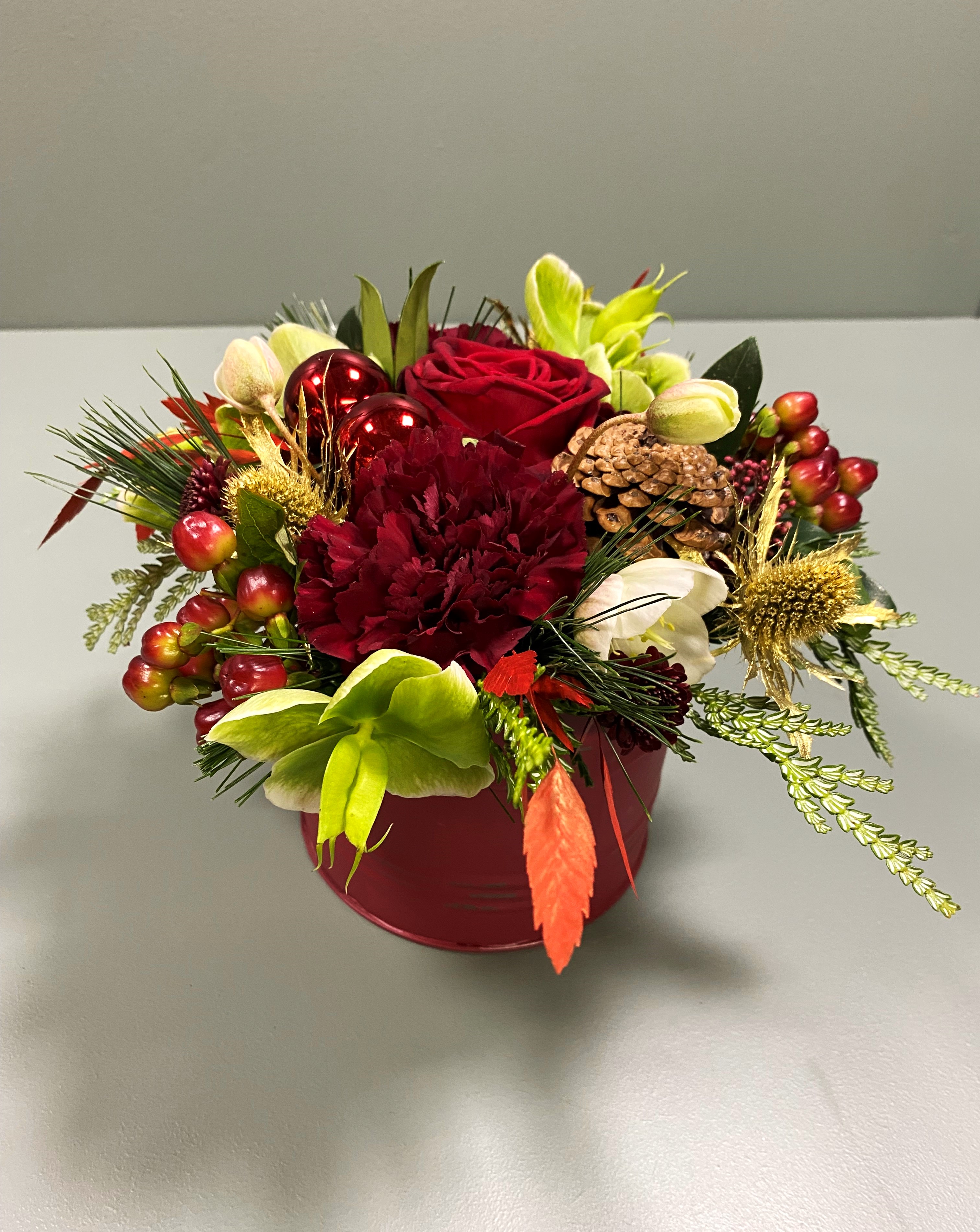 Rød dåse fyldt julekugler og julerøde blomster.