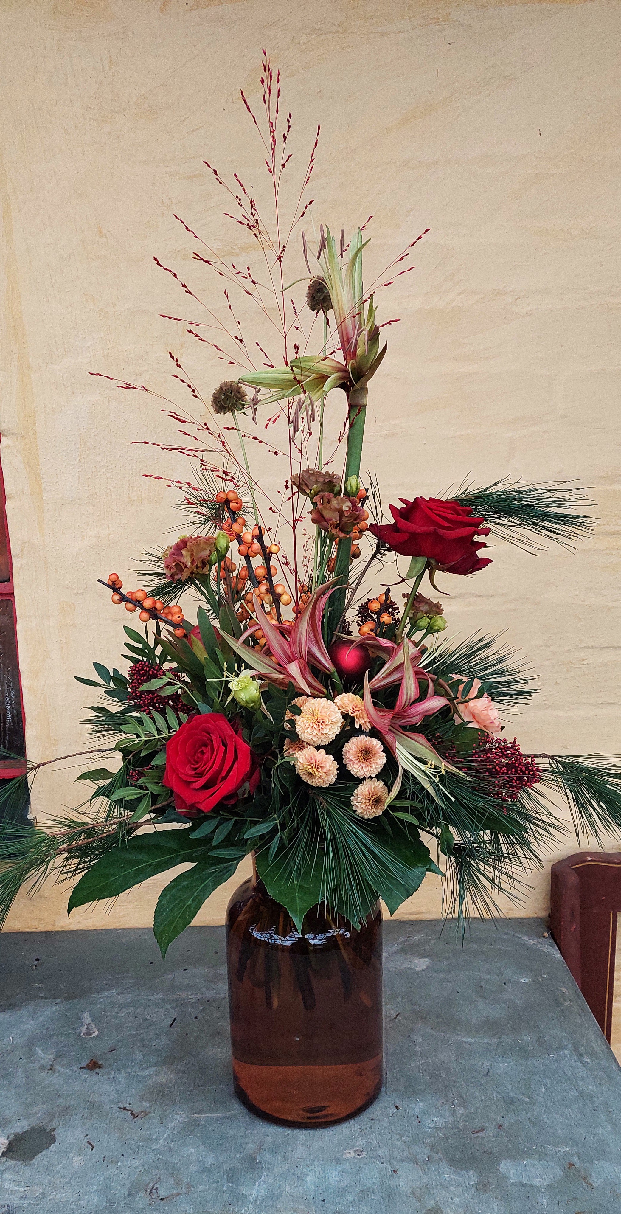 Høj julebuket med amaryllis, røde roser, gran og bærgrene. 