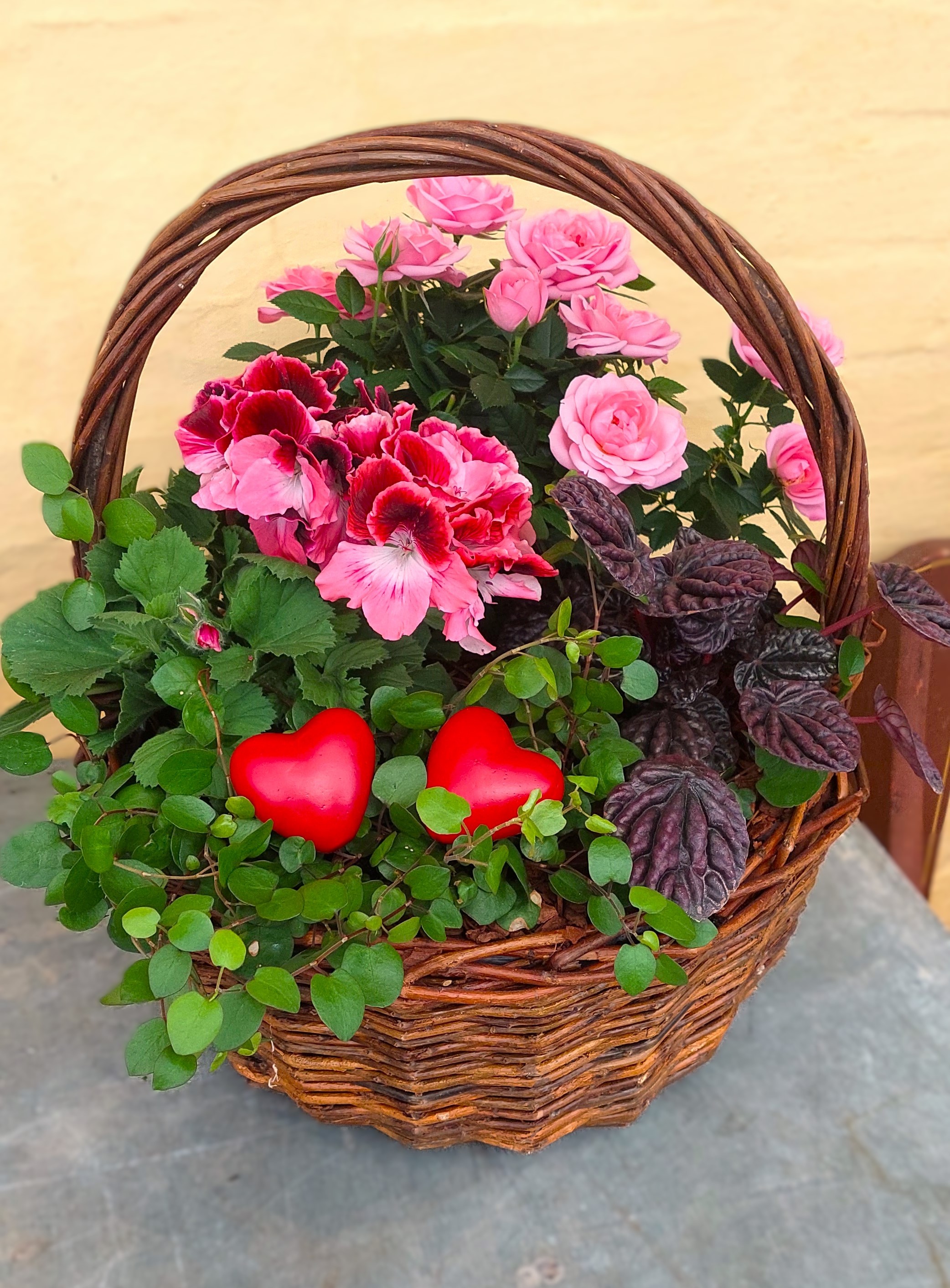 Plantearrangement i fletkurv med roser, grønne plante og pynte hjerter