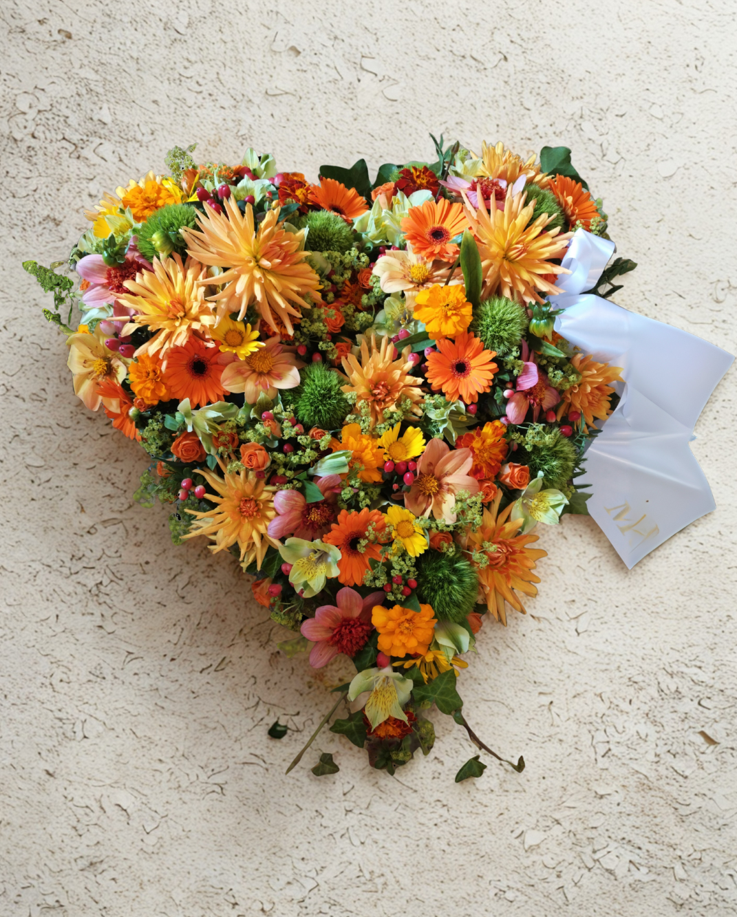 Bæredygtigt begravelseshjerte stukket med blomster i varme orange, gule, rosa og røde efterårs nuancer. 