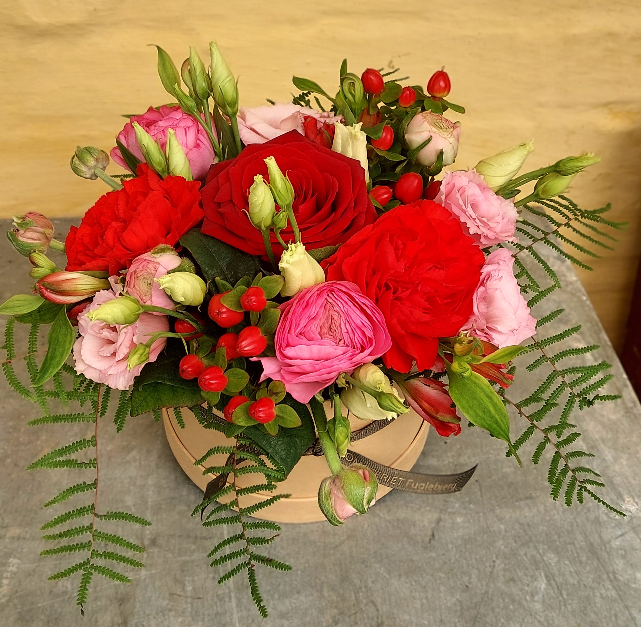 Hatteæske fyldt med røde og lyserøde roser, og rosa nelliker. 