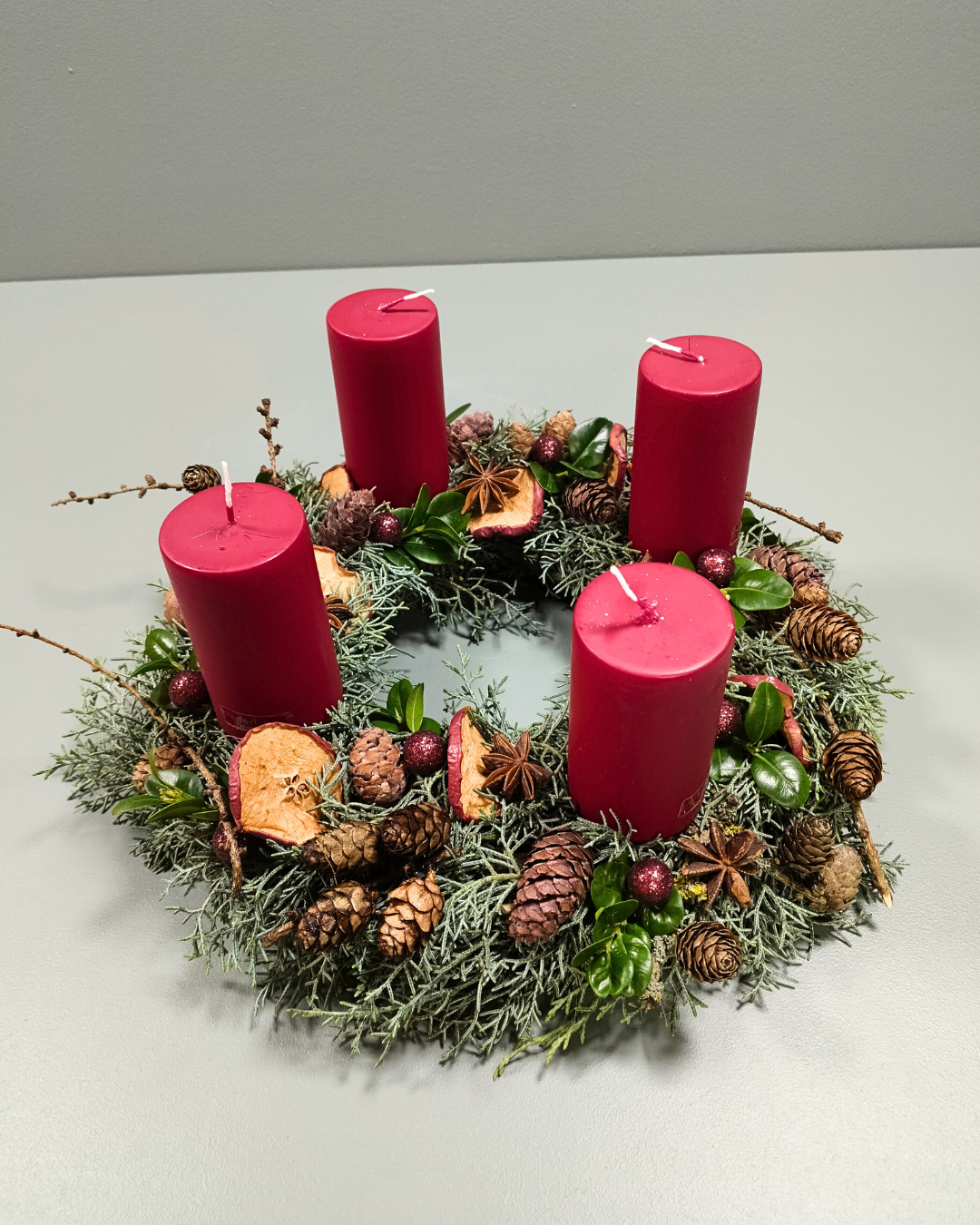 Adventskrans med røde bloklys, kogler, kran og æbleskiver. 