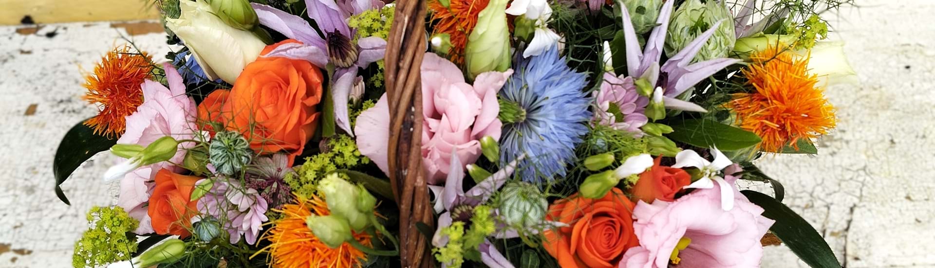 Fletkurv fyldt med sommerblomster i orange, lyserøde, lilla og blå nuancer.
